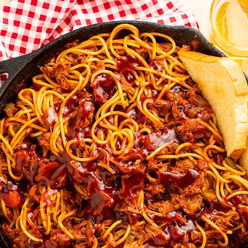 Skillet of spaghetti, pulled pork and barbecue sauce served with sliced bread and beer.