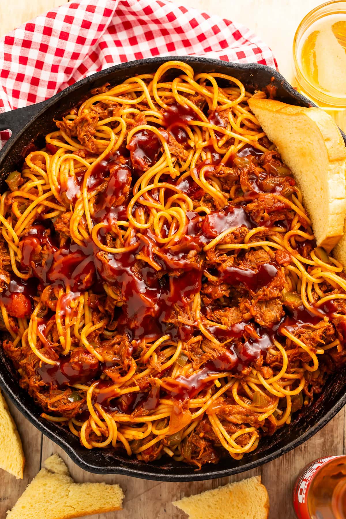 Skillet of spaghetti, pulled pork and barbecue sauce served with sliced bread and beer.