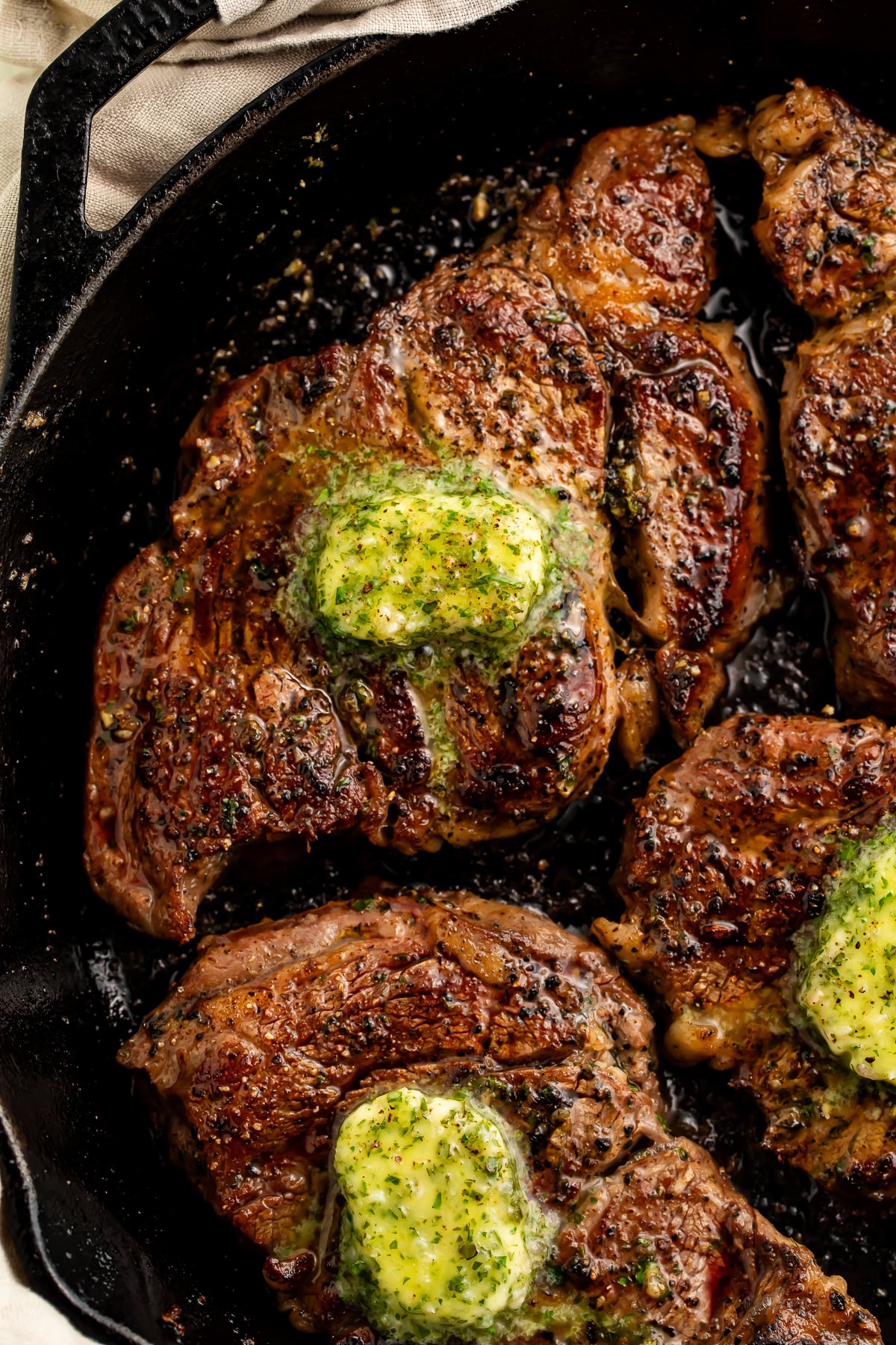 Close up of seared chuck eye steaks in a cast iron skillet topped with a garlic herb compound butter.