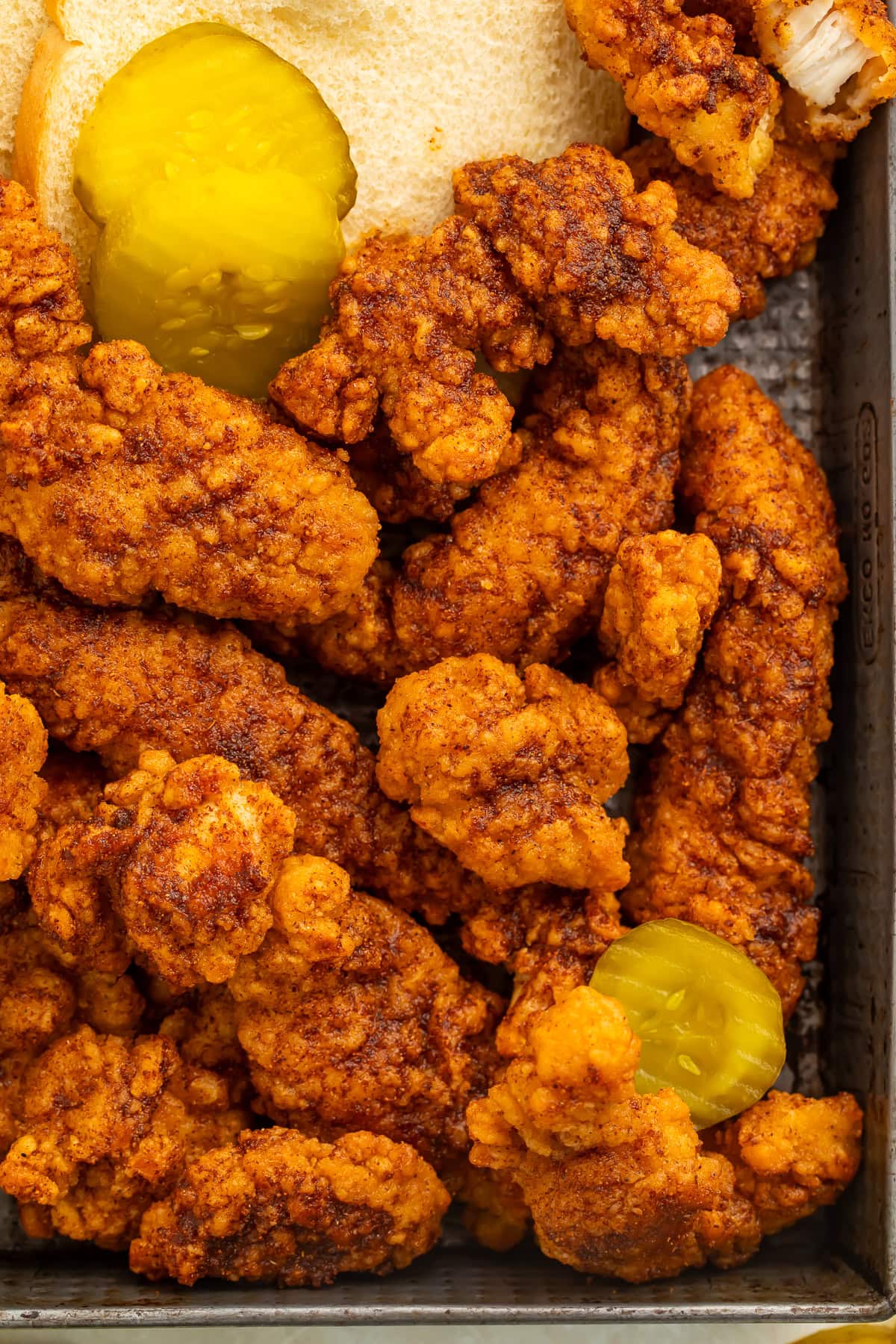 Close up of hot chicken tenders with sliced white bread and pickles.